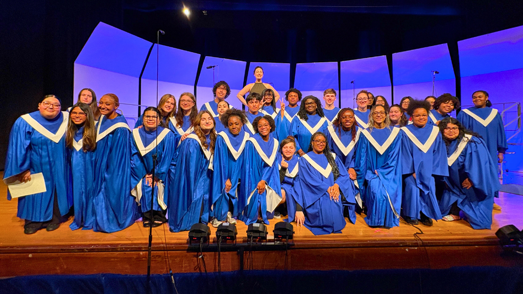 NAHS senior choir members and director pose for photo at the front of the stage.