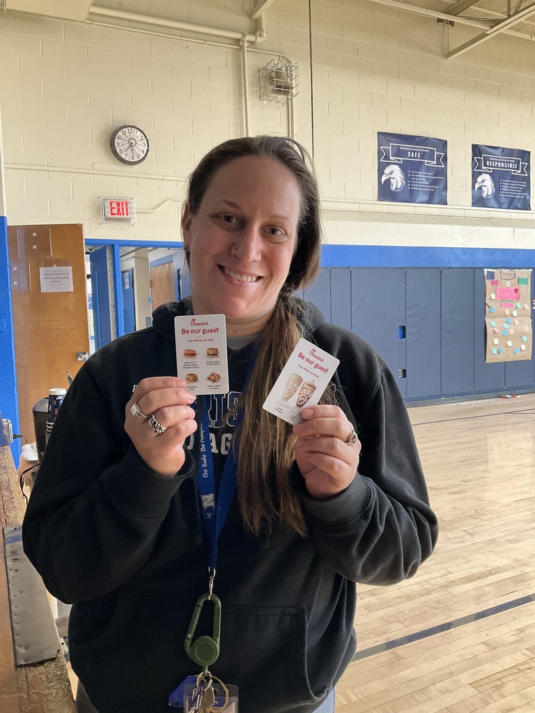 A teacher is holding two giftcards in the gym.