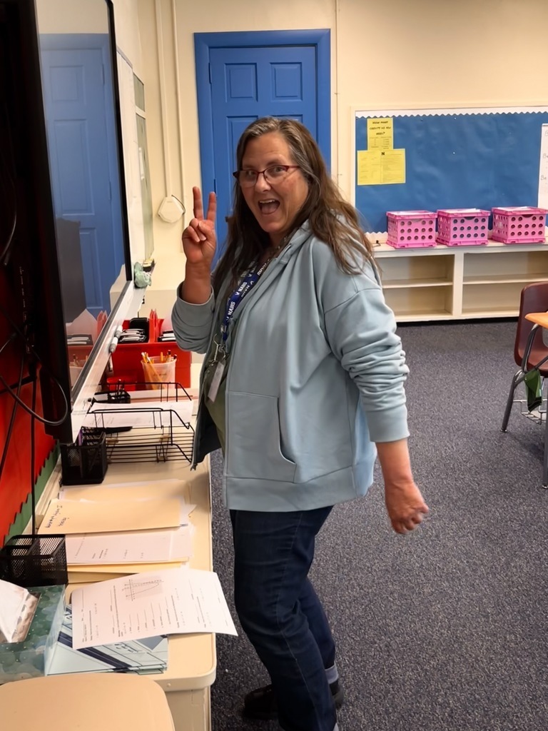 A teacher is giving the peace sign in her classroom