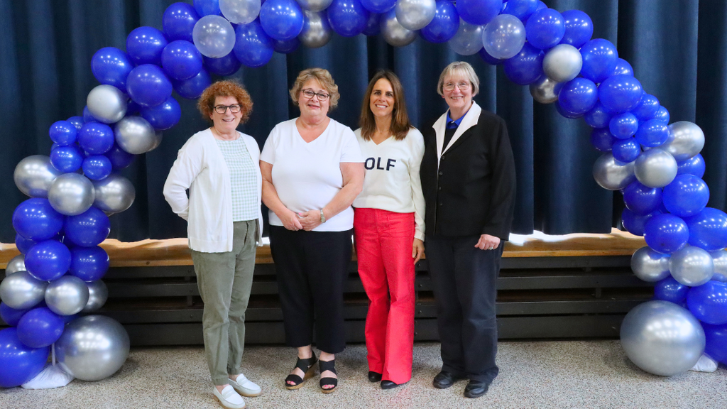 Four retirees pose for photo under blue and silver balloon arch.