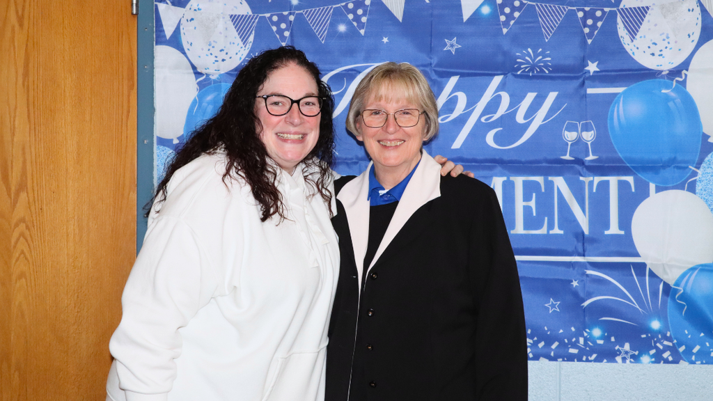 Two NASD staff members pose for photo in front of photo backdrop.