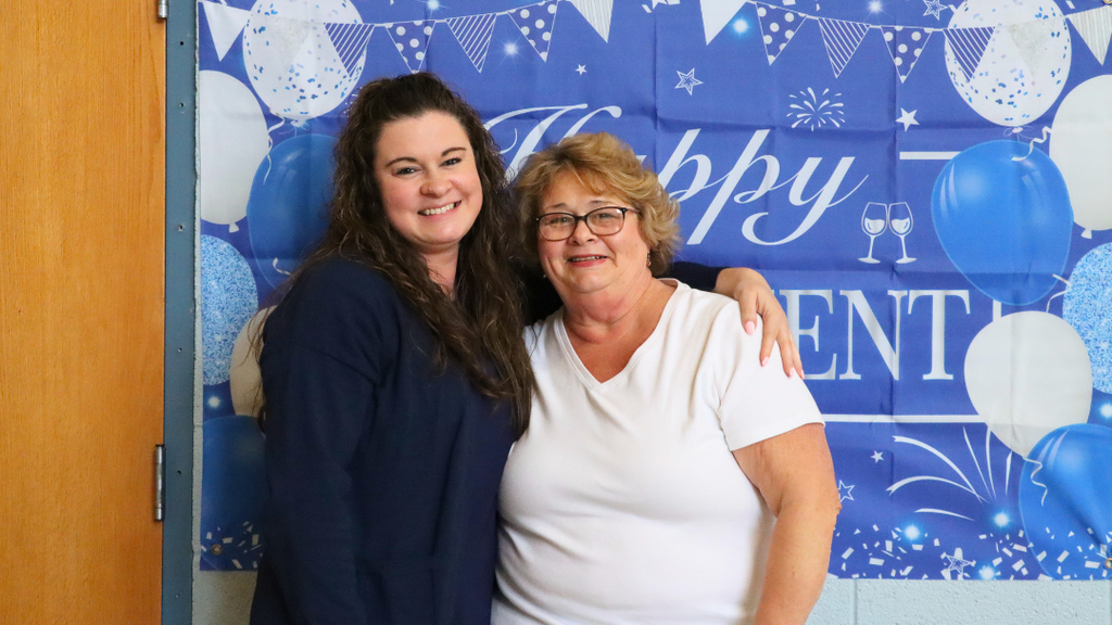 Retiree and family member pose for photo in front of photo backdrop.