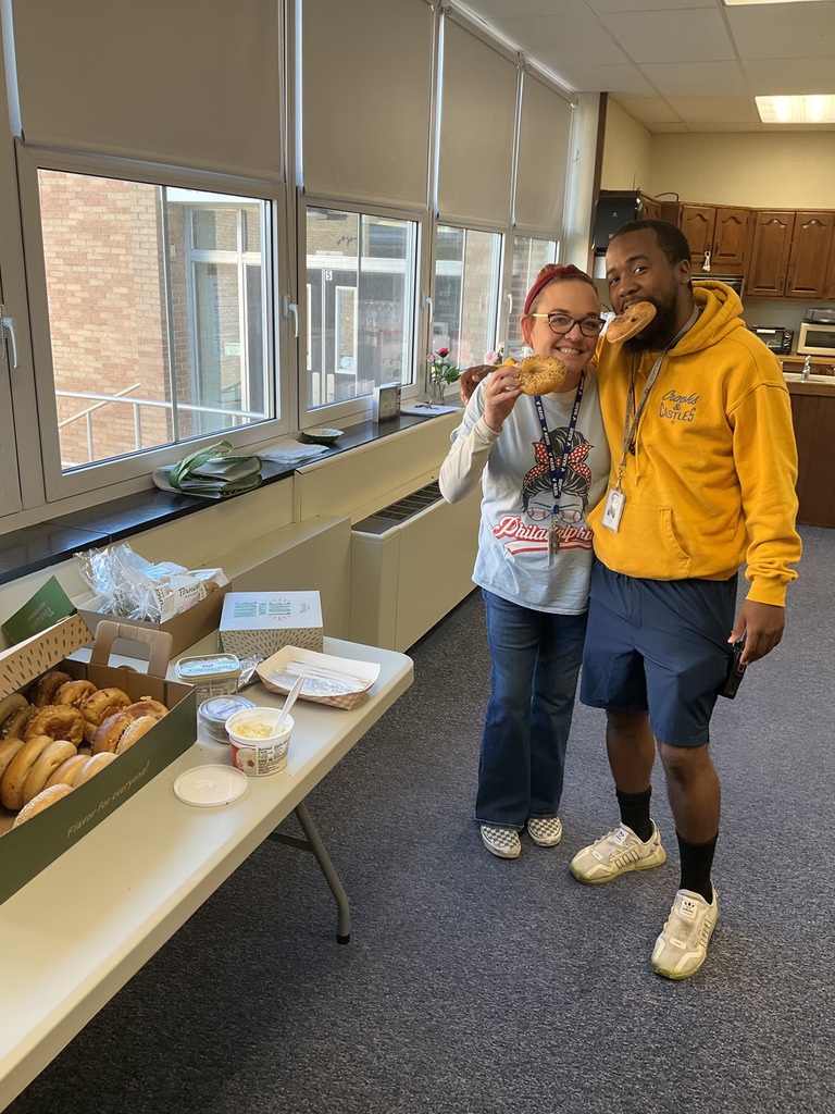 Two faculty members are posing together and eating bagels