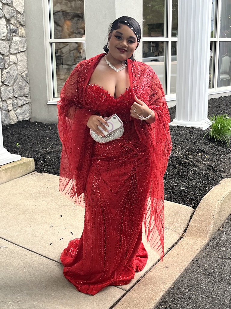 A female student is posing outside in her red gown