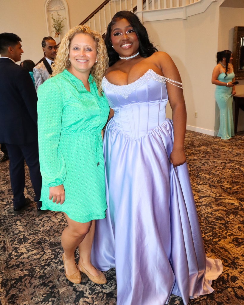 Student poses with a teacher for a photo at prom.