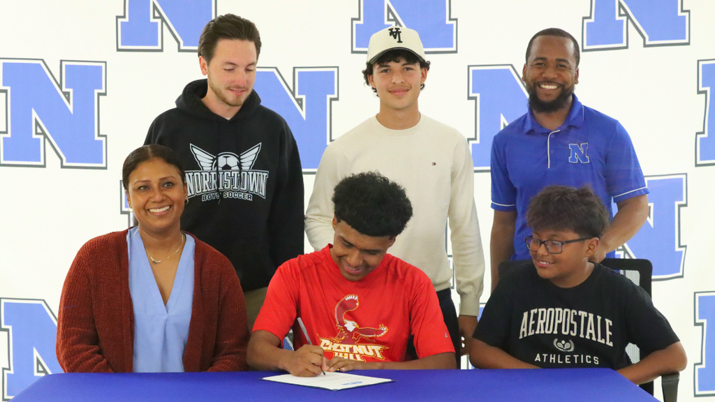 Senior student-athlete sitting at signing table with family and coaches.