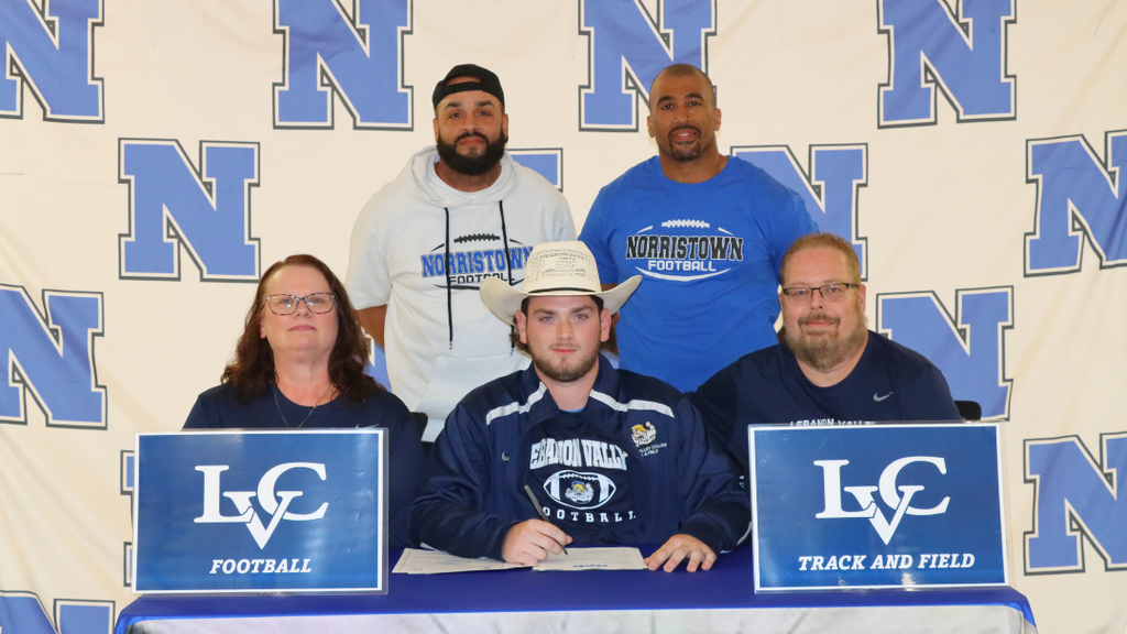 Senior student-athlete sitting at signing table with family and coaches.