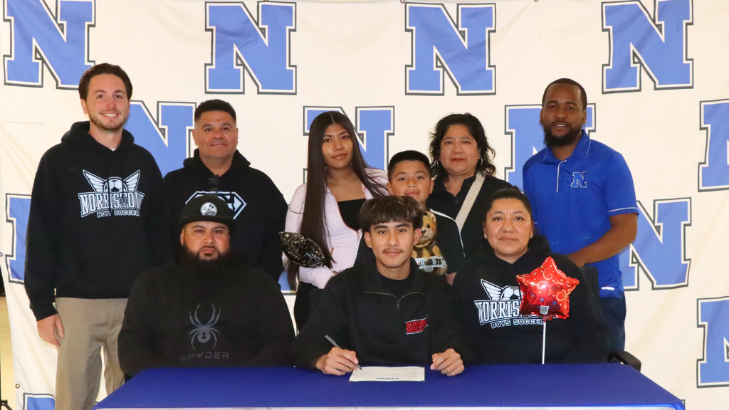 Senior student-athlete sitting at signing table with family and coaches.