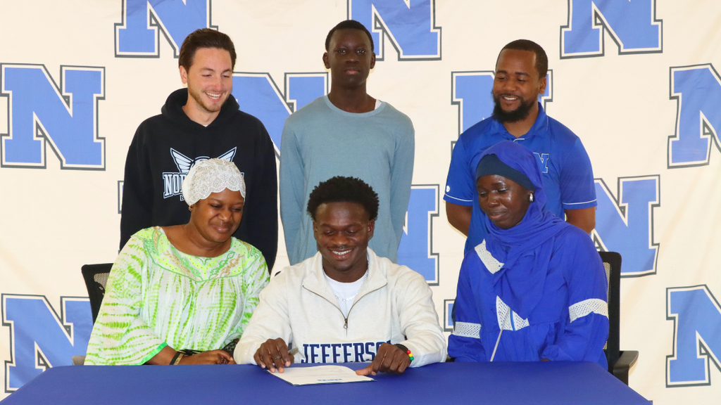 Senior student-athlete sitting at signing table with family and coaches.