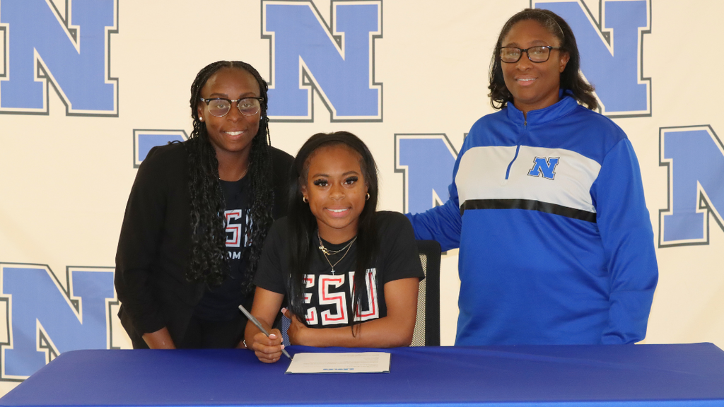Senior student-athlete sitting at signing table with family and coaches.
