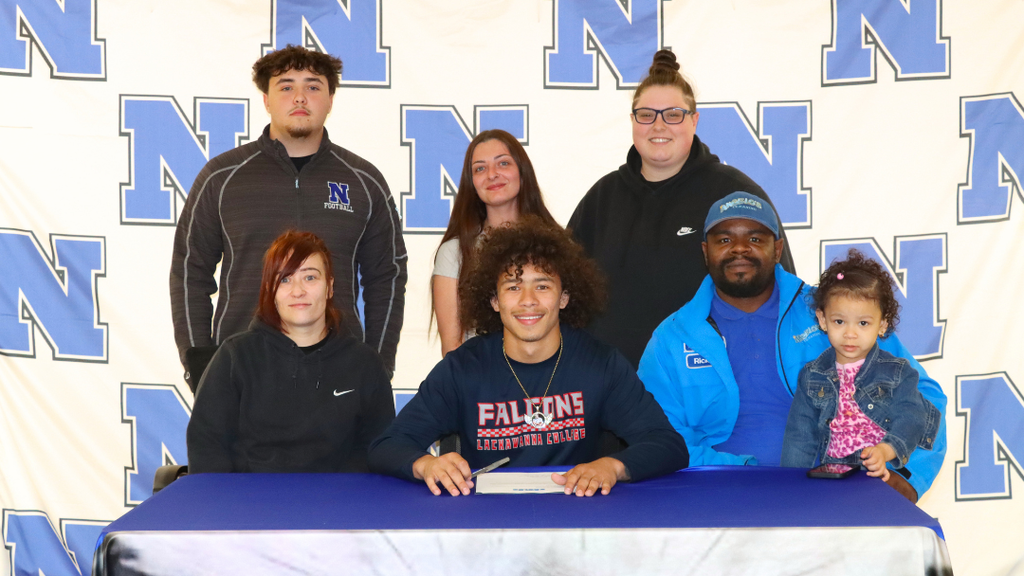 Senior student-athlete sitting at signing table with family and coaches.