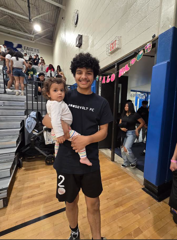 A student is holding a toddler in the school gym