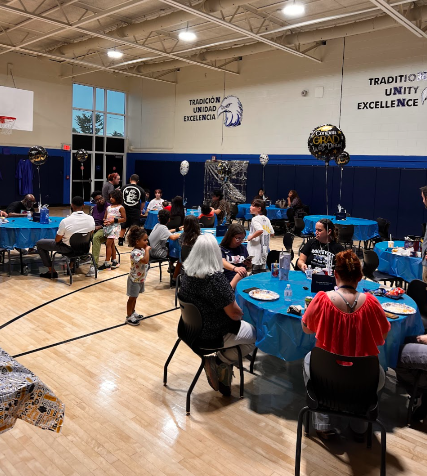 Families and staff are seated in the gym while they eat.