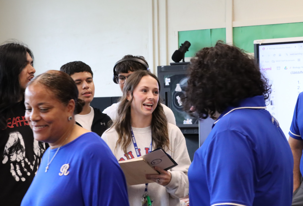 The teacher of the year is smiling with students and administration around her