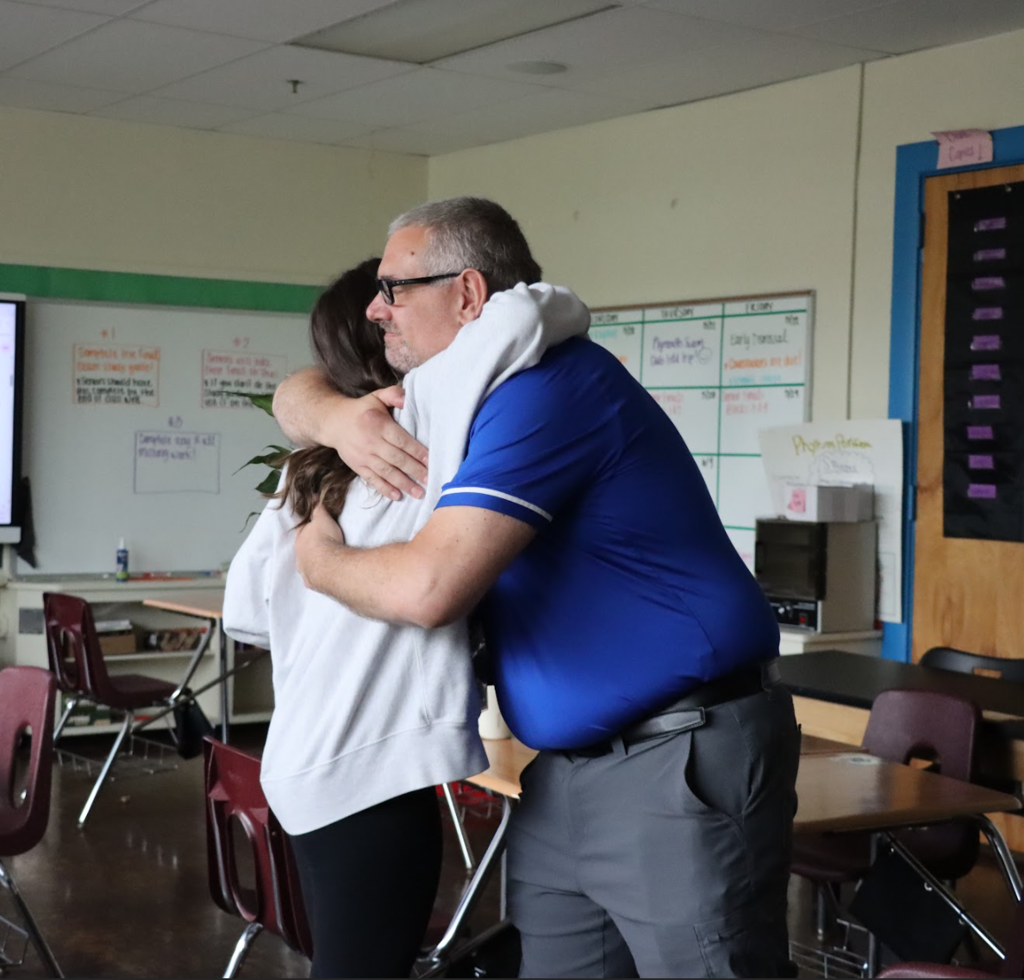 The superintendent is hugging the teacher of the year in her classroom