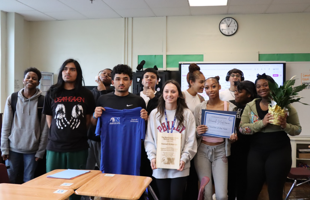 Students are gathered around the teacher of the year in her classroom and holding her awards 