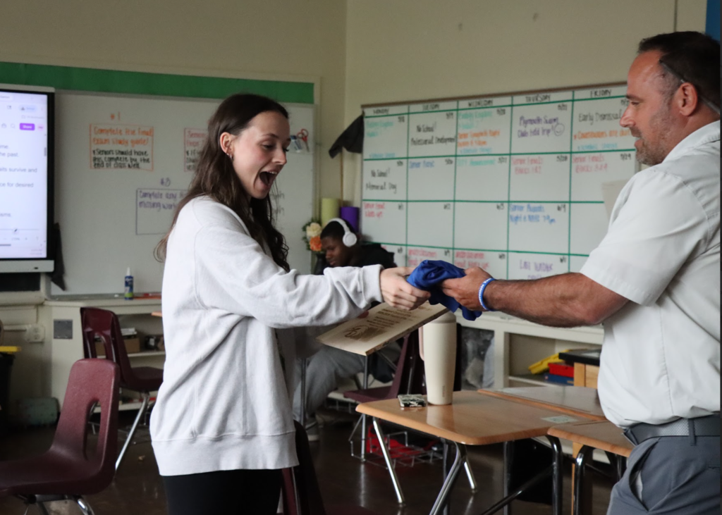 The teacher of the year is accepting her tshirt from the building principal 