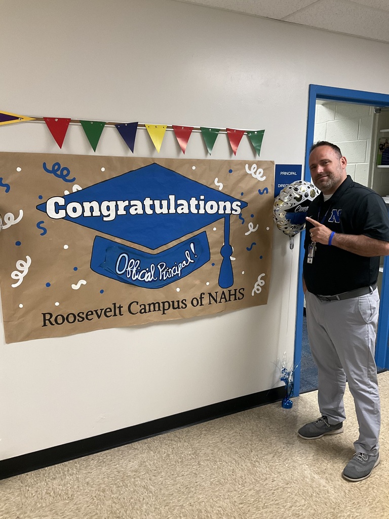 The principal is standing in front of his sign congratulating him on becoming the princpal