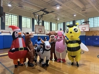 Teachers in inflatable costumes race at the field day assembly.