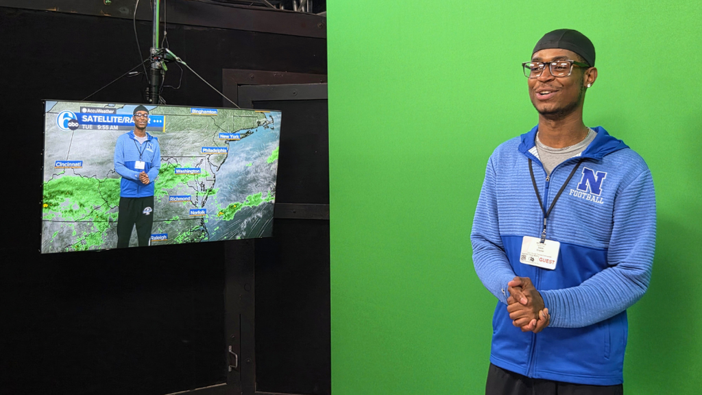 Student standing in front of green screen with a monitor of the weather map.