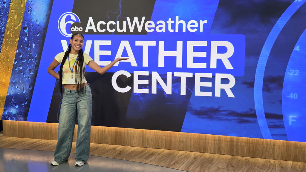 Student poses in front of the 6ABC news screen with text "AccuWeather Weather Center".