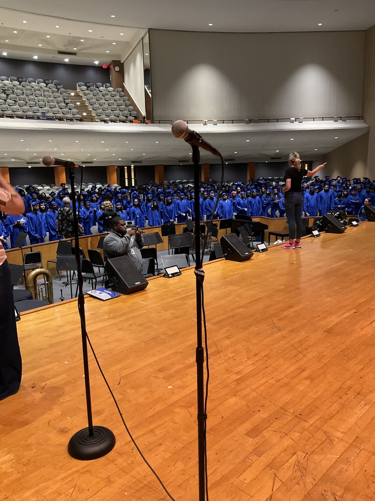 Students are standing in their cap and gowns in the auditorium