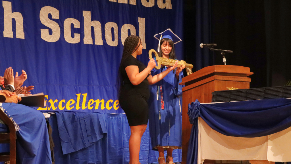 Graduate hands the NAHS Key of Knowledge to a junior class representative on stage at graduation.