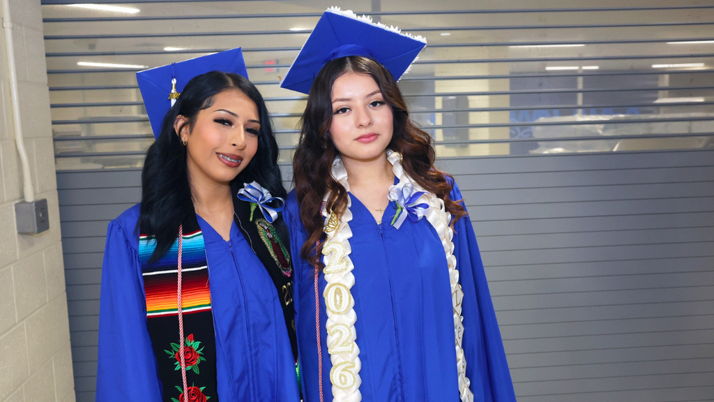 Two graduates pose for photo while waiting to line up for graduation.