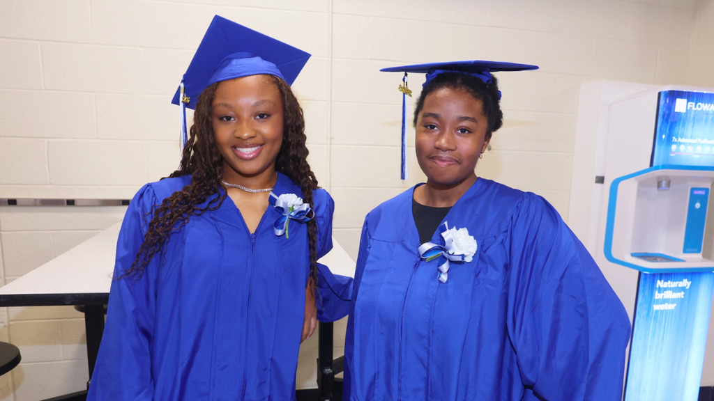 Two graduates pose for photo while waiting to line up for graduation.
