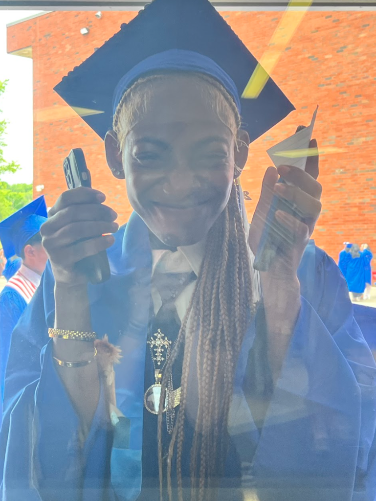 A student is peeking in the window in her cap and gown