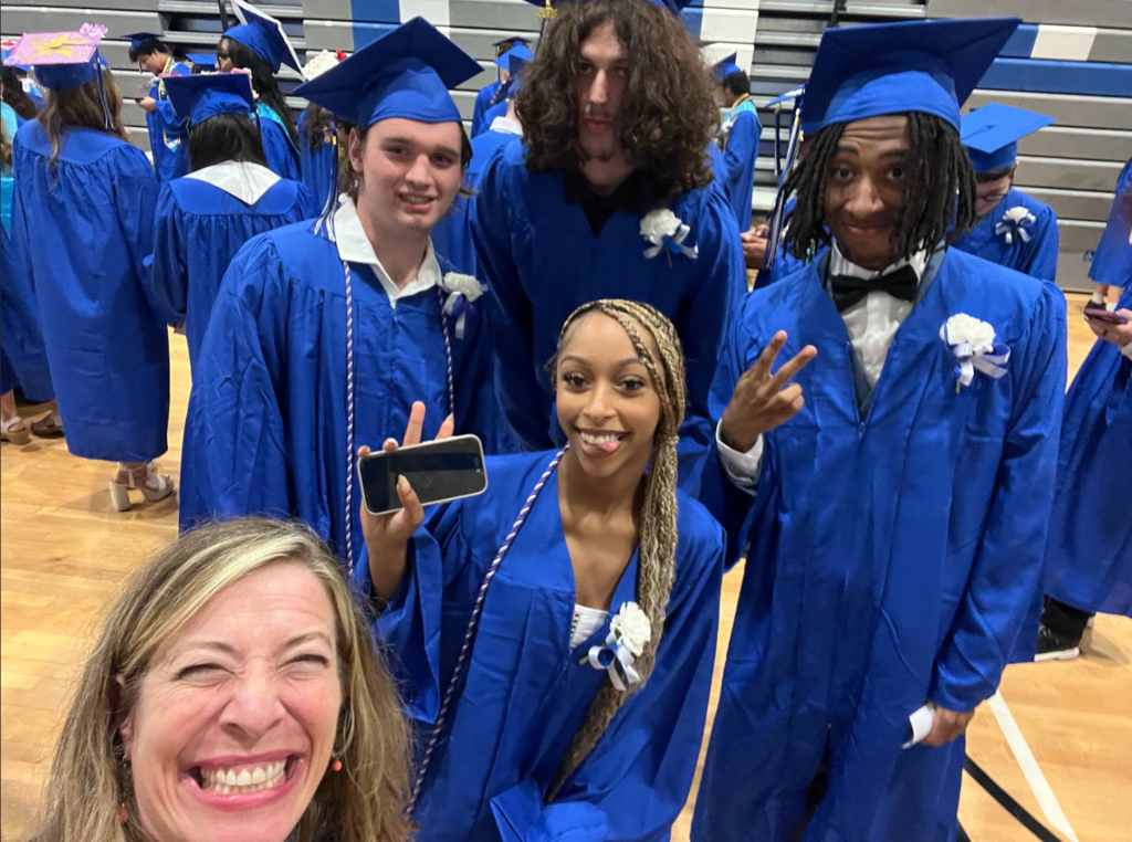Students and a teacher are gathered in their cap and gowns 