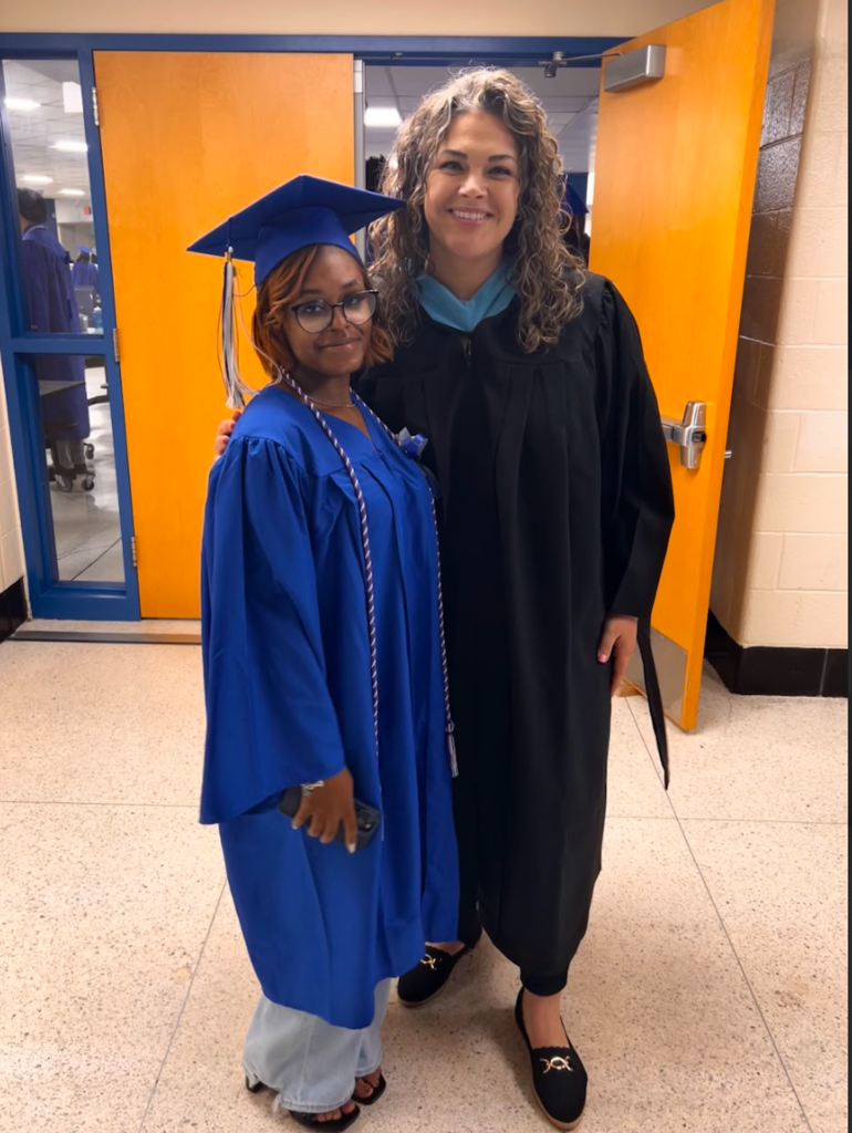 A student and teacher are posing together in their cap and gowns 