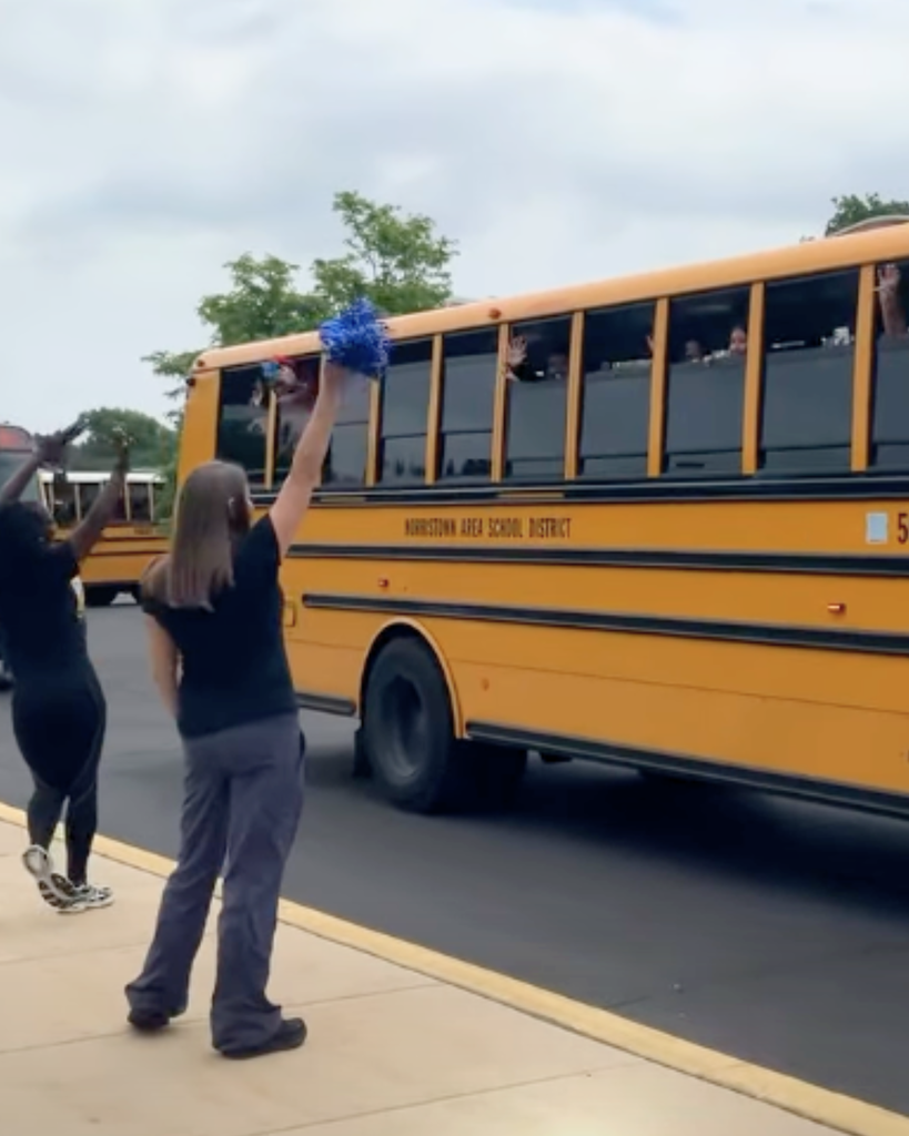 Staff waving pom poms at students on bus as they leave.