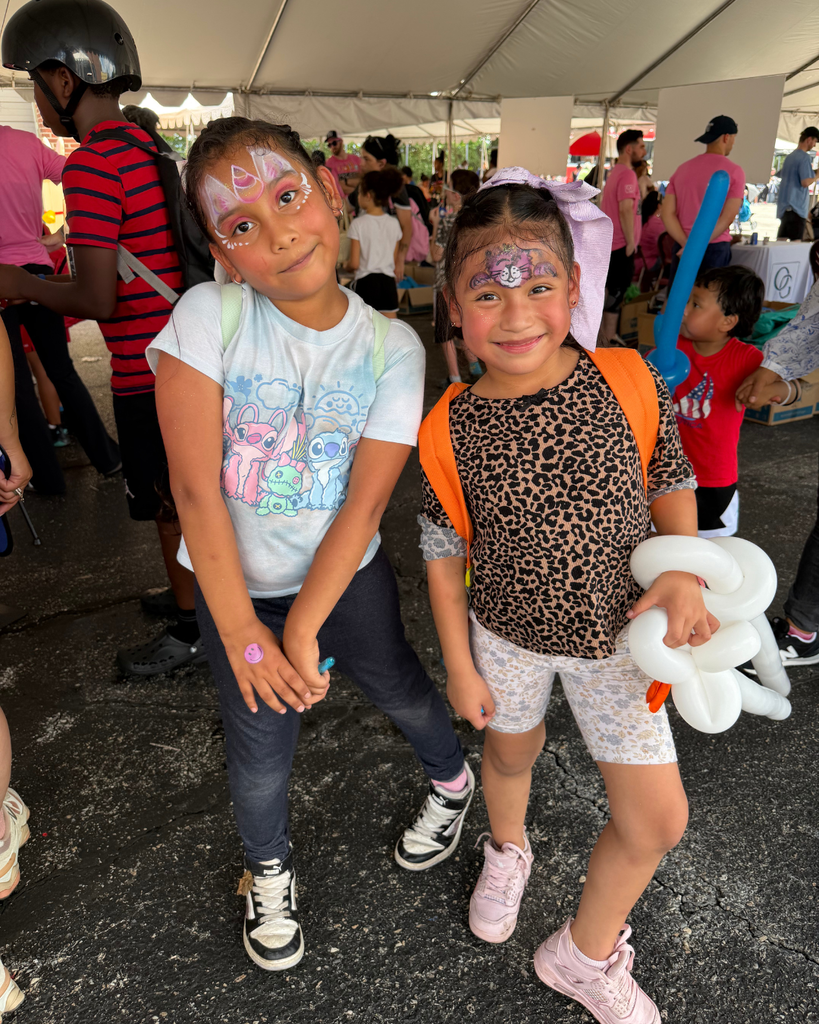 Two students with fun face paint pose for photo with their new backpacks.
