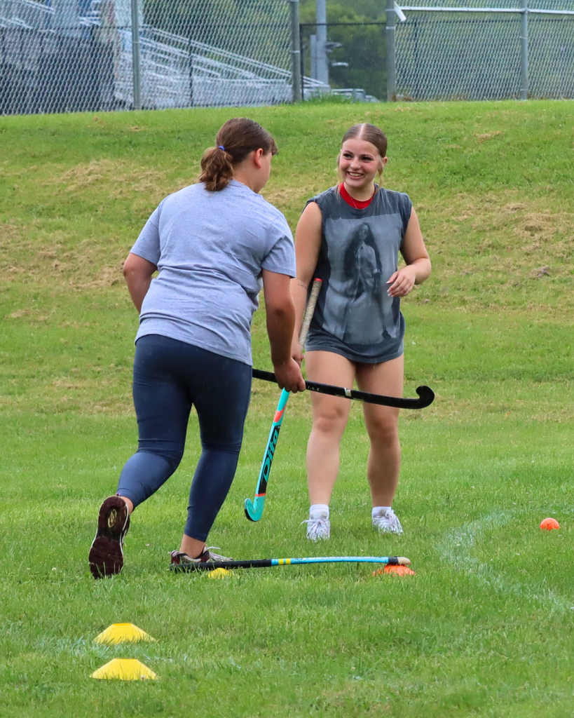 High school student athlete smiling as she helps a younger field hockey player learn the basics.