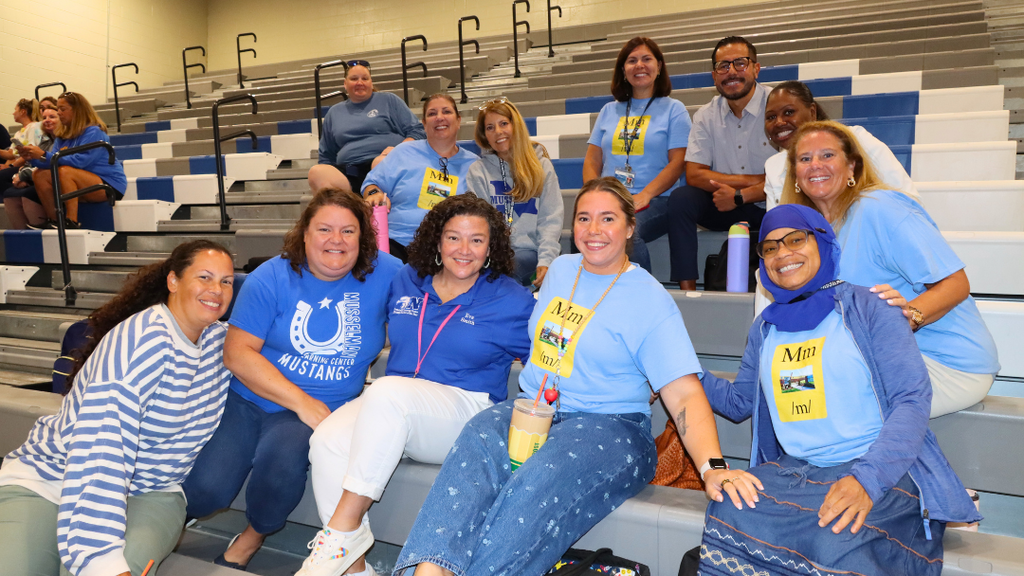 Group of teachers sitting on bleachers pose for photo before the Opening Ceremony starts.