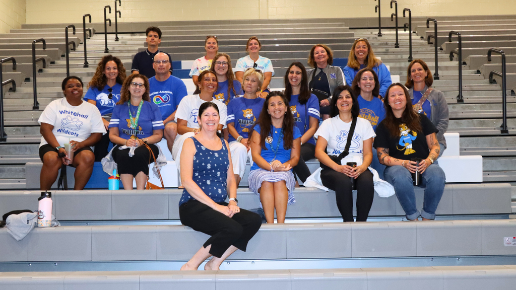 Group of teachers sitting on bleachers pose for photo before the Opening Ceremony starts.