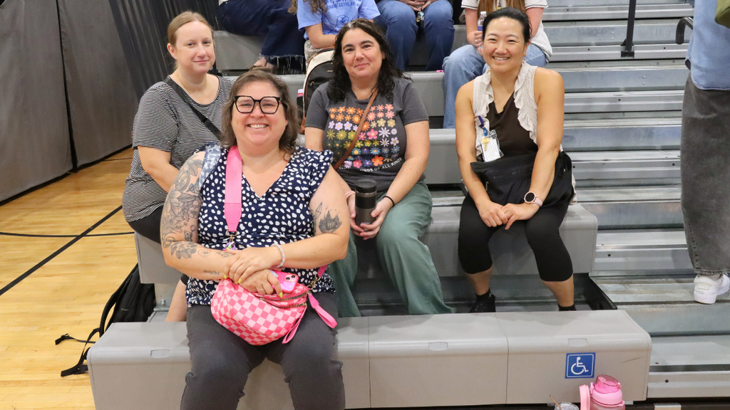 Group of teachers sitting on bleachers pose for photo before the Opening Ceremony starts.