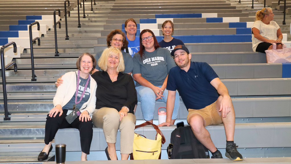 Group of teachers and staff sitting on bleachers pose for photo before the Opening Ceremony starts.