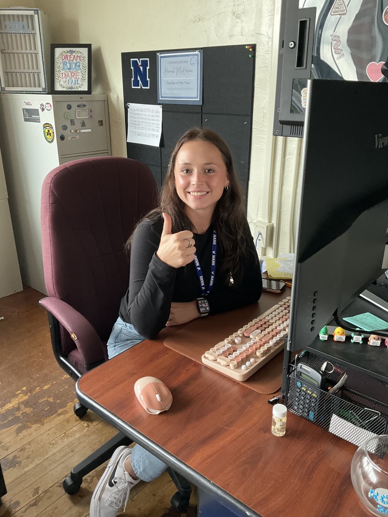 A teacher is giving a thumbs up at her desk