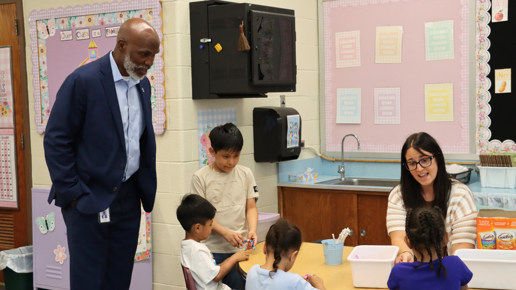 Teacher sitting at table with students with Dr. Green talks to them.