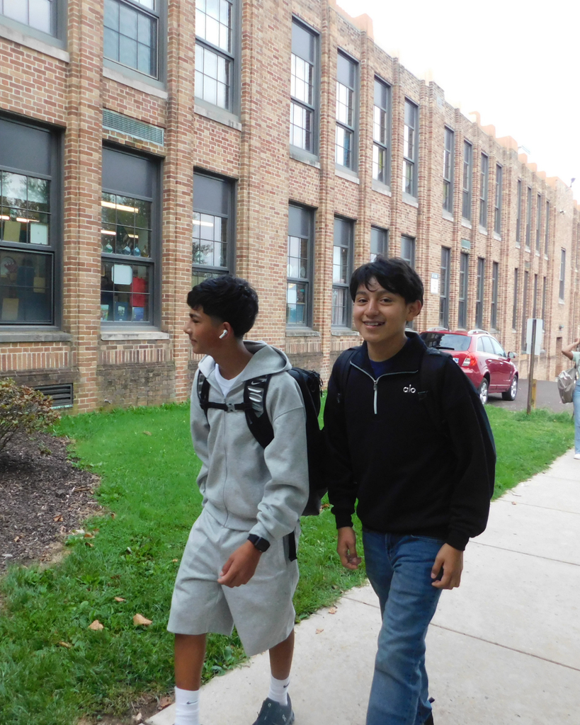 Students arriving at the building, walking on sidewalk.