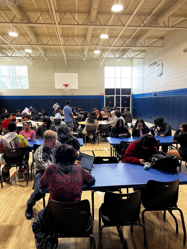 A photo of the cafeteria being full with students at lunch tables
