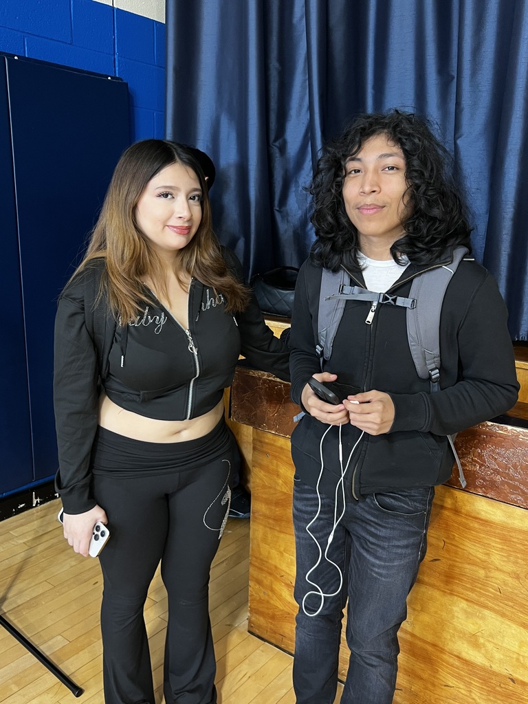 Two students are in the cafeteria together standing by the stage.