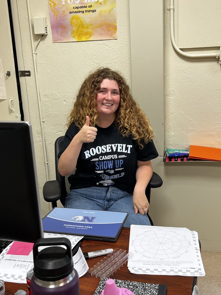 A teacher is giving a thumbs up from her desk