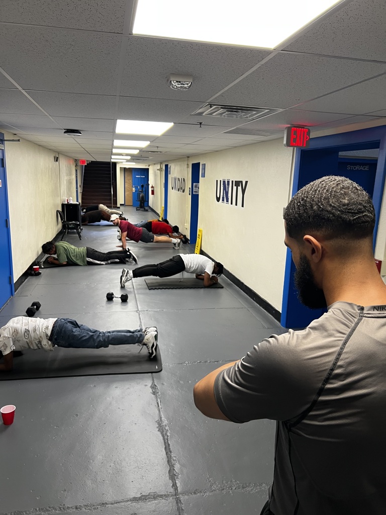 The coach is looking at his watch at students doing planks on the ground