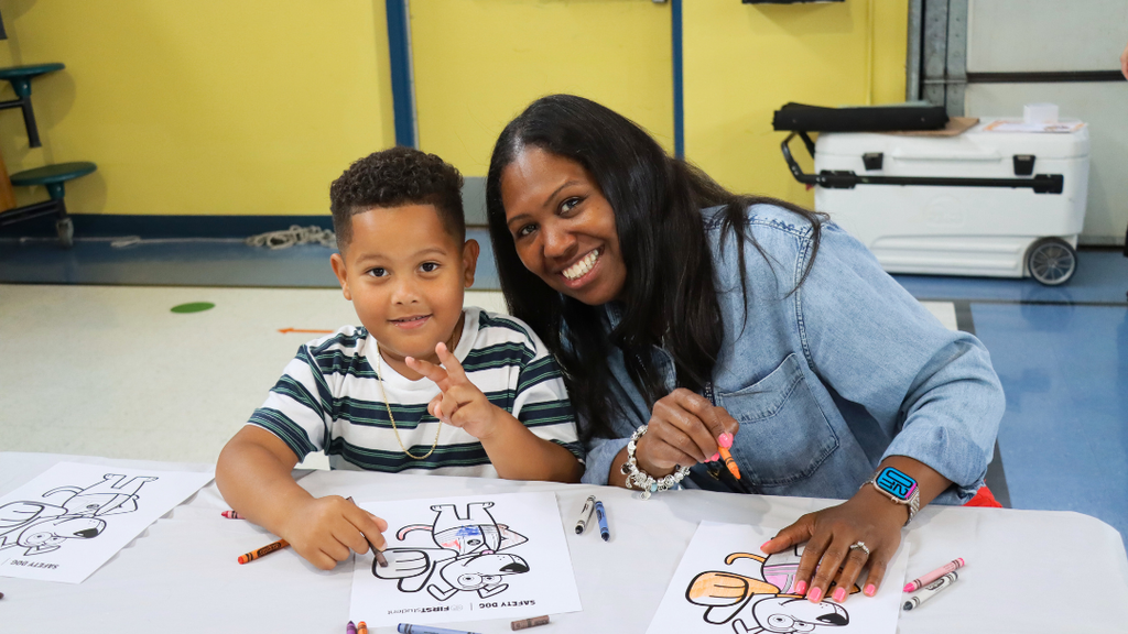Student and staff member smile for photo while coloring a page with Safety Dog.