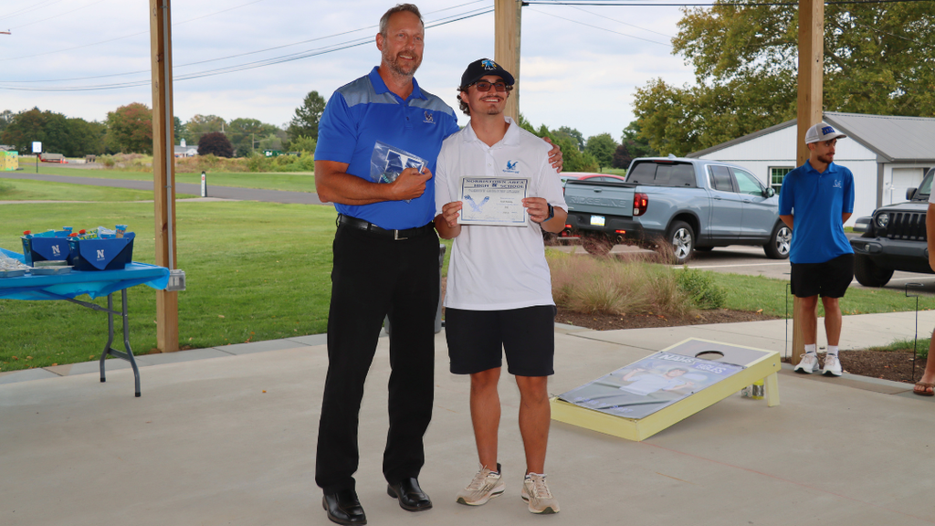 Senior athlete and coach pose for photo with certificate and varsity letter.