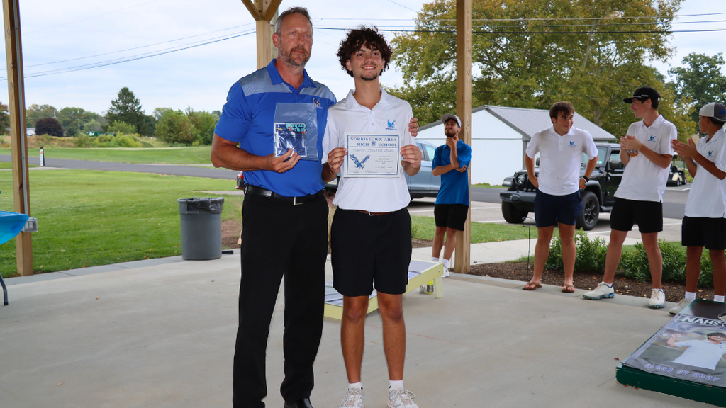 Senior athlete and coach pose for photo with certificate and varsity letter.