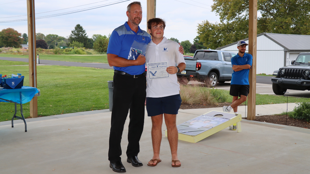 Senior athlete and coach pose for photo with certificate and varsity letter.
